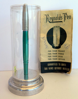 4586: REYNOLDS INTERNATIONAL BALLPOINT IN CHROME GREEN WITH ALUMINUM CAP WITH CIRCUMFERENTIAL GROVES. THE CAP REMOVES AND SNAPS ON OVER THE FRONT END OF THE PEN. COMES WITH PAPER INSTRUCTIONS AND GUARENTEE. CONTAINS A VERY CLEAR CELLOPHANE COVER AND AN ALUMINUM PEDISTOOL. ALL ITEMS FIT INSIDE AND ELABORATE DISPLAY CASE IN LIGHT BLUE VELVENTEEN